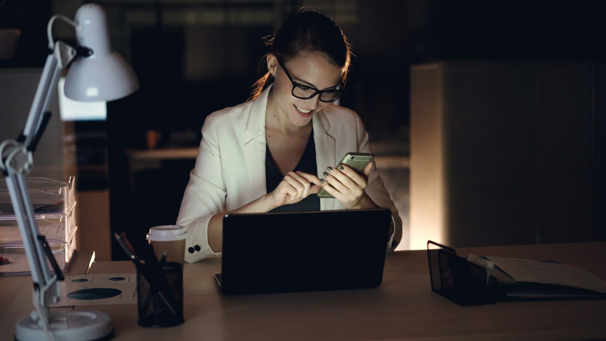 A marketer reviewing campaign results on a laptop and phone in the evening
