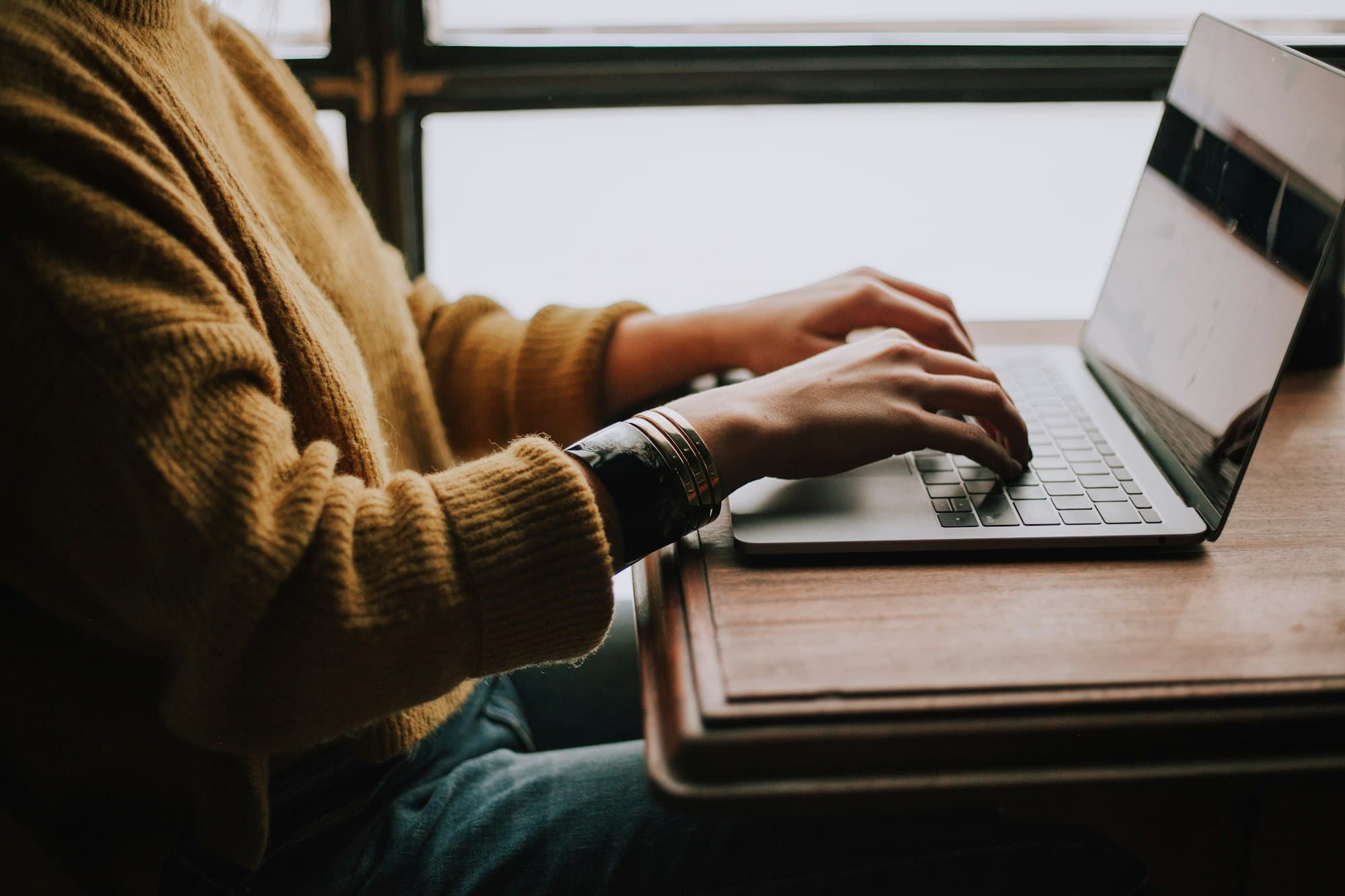 A professional reading a report on a laptop at a wooden desk